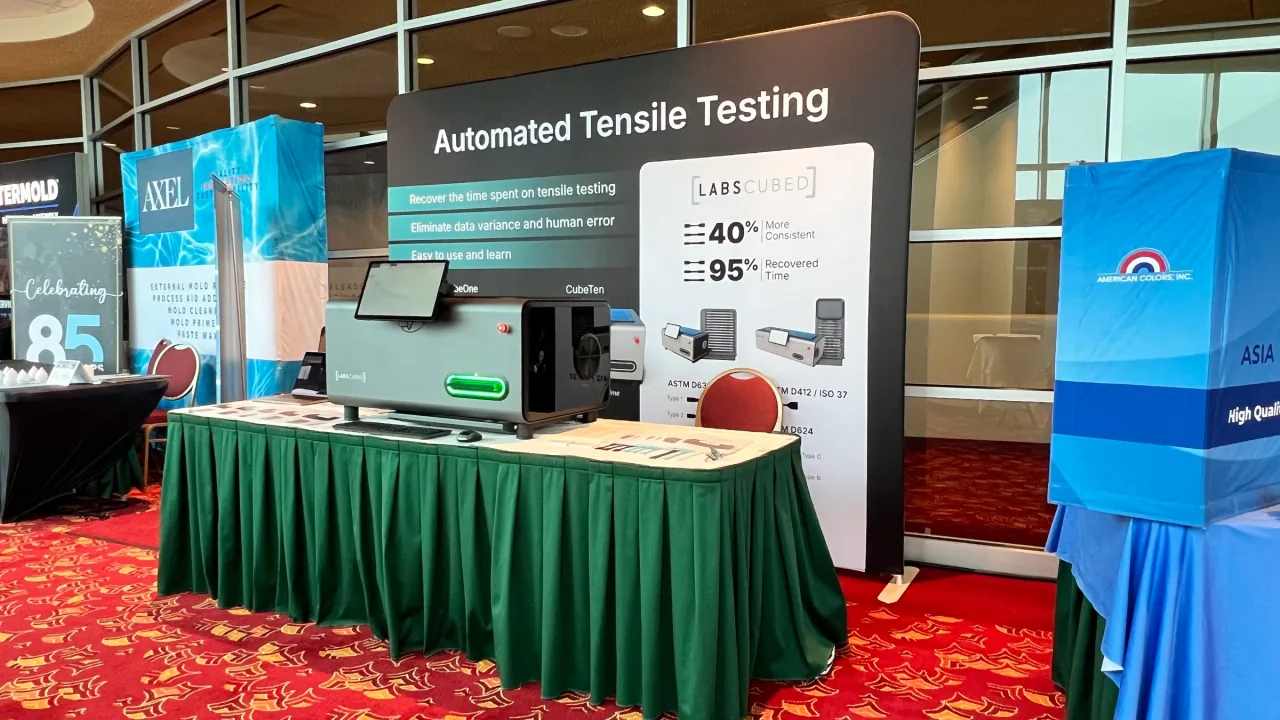 LabsCubed CubeTen automated plastic tensile testing machine at a trade show booth.